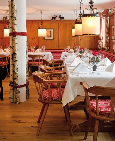Rustikaler Restaurantbereich mit Holzmöbeln, weiß gedeckten Tischen und Hängeleuchten an holzvertäfelten Wänden.