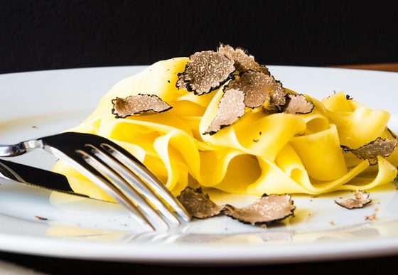 Breite Tagliatelle auf weißem Teller mit Trüffelscheiben und Gabel.