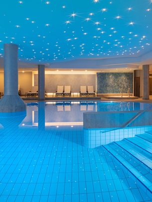 Innenpool im Wellnessbereich mit Sternenhimmel-Decke, Einstiegstreppe, Säulen und Ruheliegen.