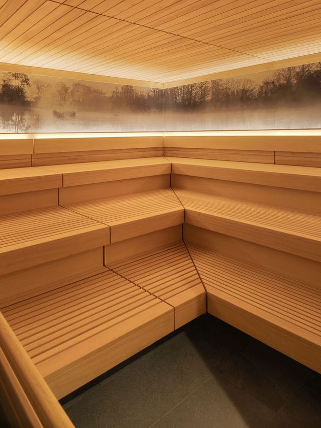 Innenansicht einer Sauna mit Holzbänken, Saunaofen und indirekter Beleuchtung an der Wand.