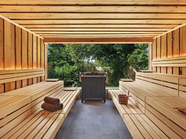 Innenansicht einer Holzsauna mit Sitzbänken, Saunaofen und offenem Blick in den Garten.