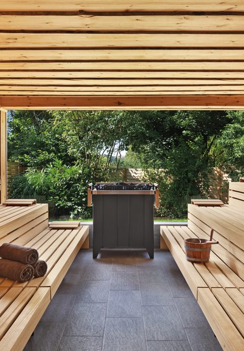 Innenansicht einer Holzsauna mit Sitzbänken, Saunaofen und offenem Blick in den Garten.