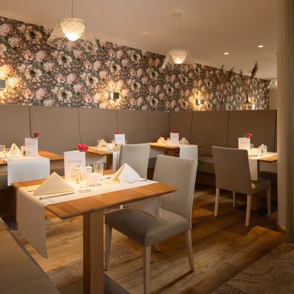 Restaurantbereich mit gedeckten Tischen, gepolsterter Sitzbank und floraler Tapete im Innenraum.