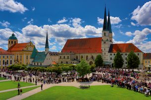 Historische Kirche mit hohen Türmen und Menschenmenge auf einem großen Platz unter blauem Himmel.