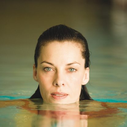 Nahaufnahme einer Frau im Pool mit Gesicht über der Wasseroberfläche und Spiegelung im Wasser.