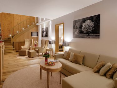 Wohnbereich einer Suite mit Sofa, Sesseln, Couchtisch und Holztreppe im Innenraum.