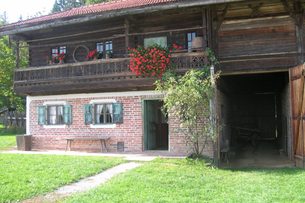 Traditionelles Bauernhaus mit Holzbalkon, Blumenkästen, Ziegeldach und Garten vor dem Gebäude.