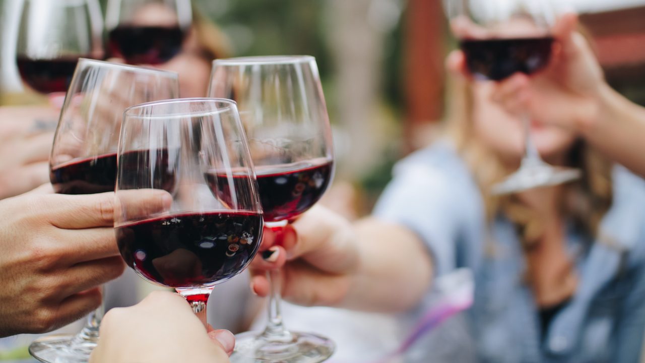 Mehrere Gäste stoßen im Außenbereich mit Gläsern Rotwein an.