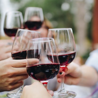 Mehrere Gäste stoßen im Außenbereich mit Gläsern Rotwein an.