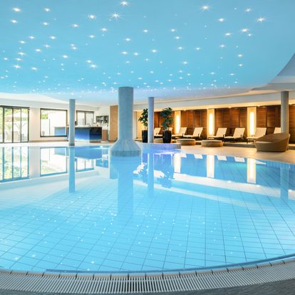 Großer Innenpool im Wellnessbereich mit Liegen, Säulen und beleuchteter Decke.