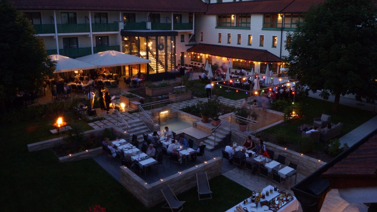 Hotel courtyard with terrace, set tables, string lights and guests in the evening.