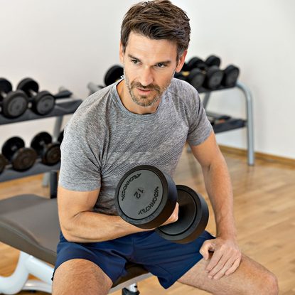 Ein Mann trainiert im Fitnessraum sitzend mit einer Kurzhantel auf einer Hantelbank.