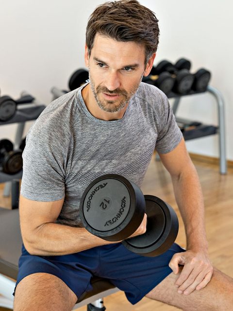 Ein Mann trainiert im Fitnessraum sitzend mit einer Kurzhantel auf einer Hantelbank.