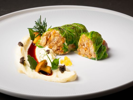 Aufgeschnittene Wirsingroulade mit Püree, Sauce und Garnitur auf einem weißen Teller.
