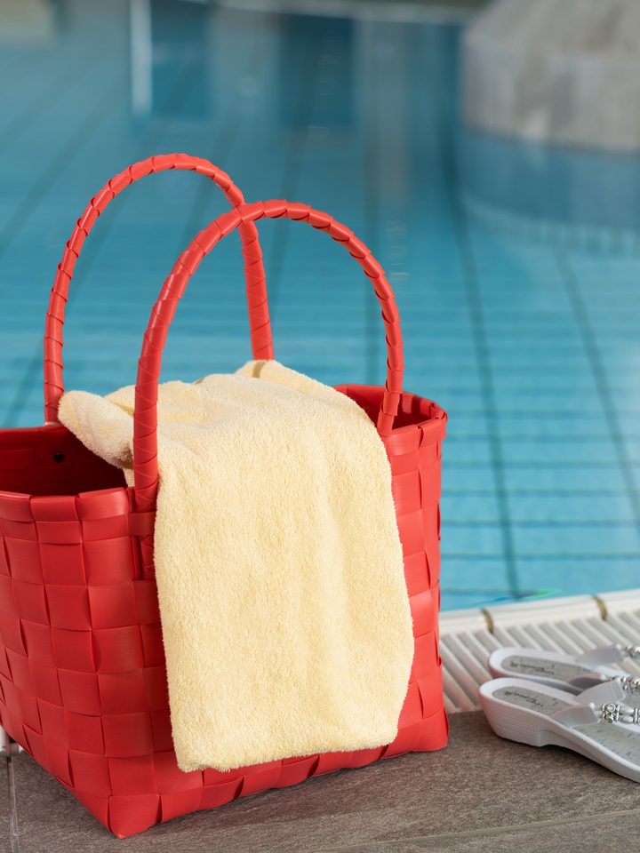 Red bag with yellow towel and flip-flops at the edge of an indoor pool.