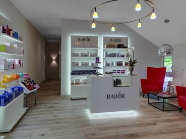 Moderner Kosmetikbereich mit beleuchteten Regalen, Babor-Theke und roten Sesseln im Innenraum.
