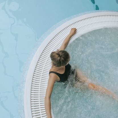 Frau im schwarzen Badeanzug entspannt in einem runden Whirlpool mit sprudelndem Wasser.