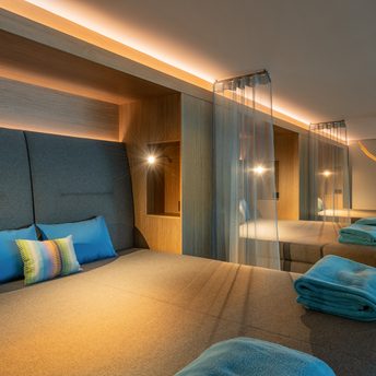 Moderner Wellness-Ruheraum mit mehreren gepolsterten Liegen, Kissen, Handtüchern und indirekter Beleuchtung.