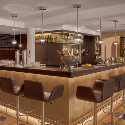 Moderne Hotelbar mit beleuchteter Bartheke, Barhockern, Flaschenregalen und Champagnerkühler.