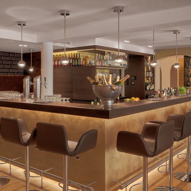 Moderne Hotelbar mit beleuchteter Bartheke, Barhockern, Flaschenregalen und Champagnerkühler.