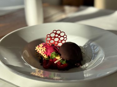 Dessert mit Schokoladenkugel, Beerensorbet, Himbeeren und Dekor auf einem weißen tiefen Teller.