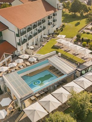 Luftaufnahme eines Hotels mit Außenpool, Sonnenterrasse, Garten und Liegebereichen.
