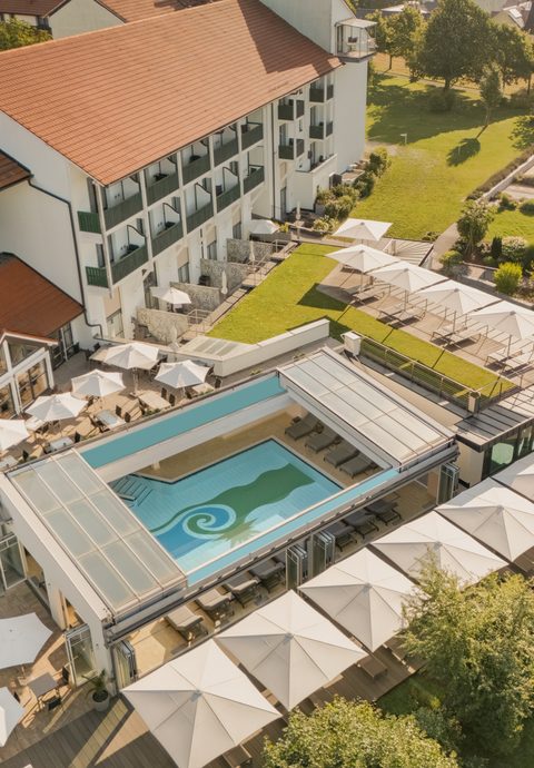 Luftaufnahme eines Hotels mit Außenpool, Sonnenterrasse, Garten und Liegebereichen.