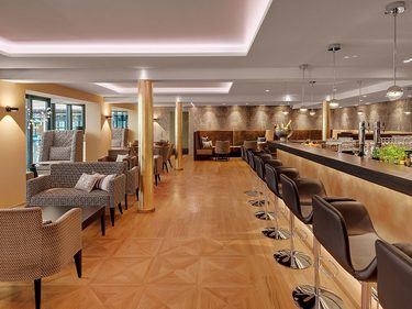 Moderne Hotelbar mit langem Tresen, Barhockern und Sitzgruppen in einem warm beleuchteten Innenraum.