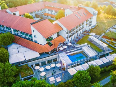 Luftaufnahme einer Hotelanlage mit roten Dächern, Außenpool, Terrassen und Gartenbereichen.
