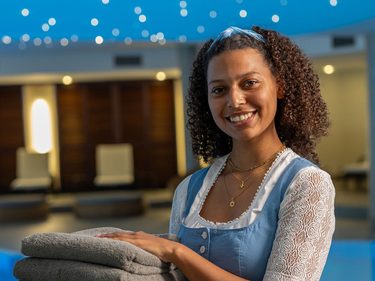 Mitarbeiterin mit gefalteten Handtüchern steht im Wellnessbereich vor einem Innenpool.