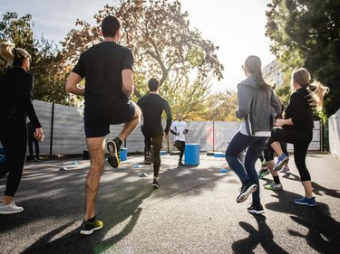 Eine Gruppe macht Aufwärmübungen bei einem Outdoor-Fitnesstraining auf einem asphaltierten Platz.