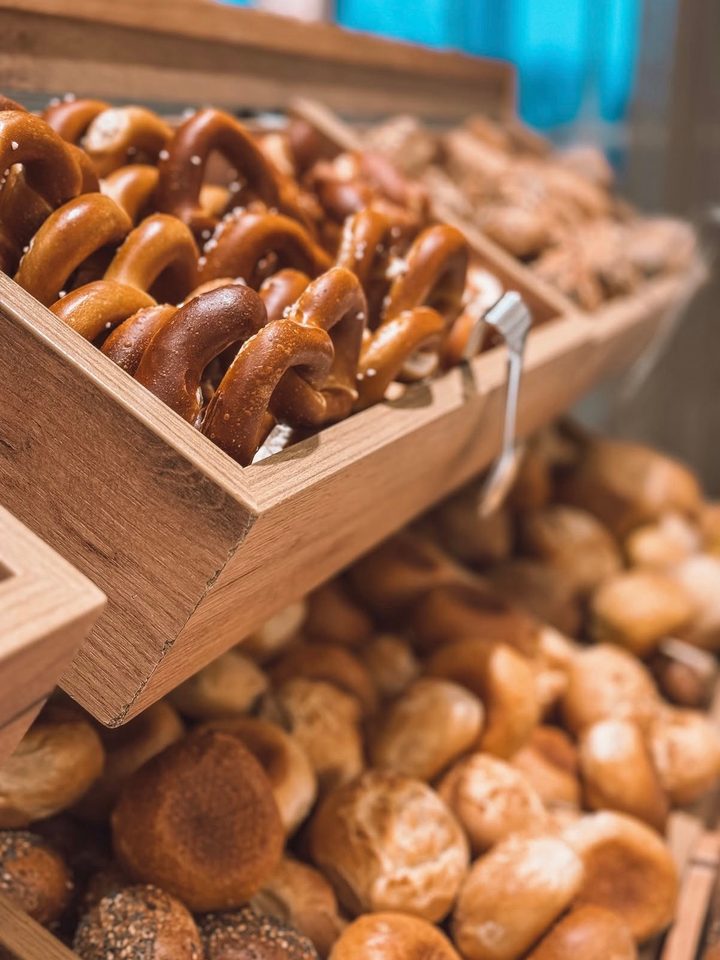 Pretzels, bread rolls and pastries in wooden trays at a breakfast buffet.