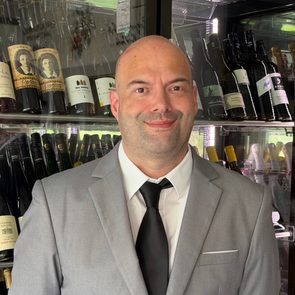 Ein Mitarbeiter im Anzug steht vor einem gekühlten Weinregal mit zahlreichen Weinflaschen.