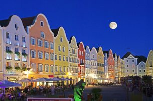 Belebter Stadtplatz mit bunten historischen Giebelhäusern, Straßencafés und Vollmond am Abend.