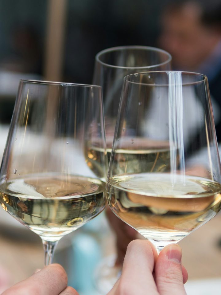 Three glasses of white wine clinking in a restaurant, held by guests.