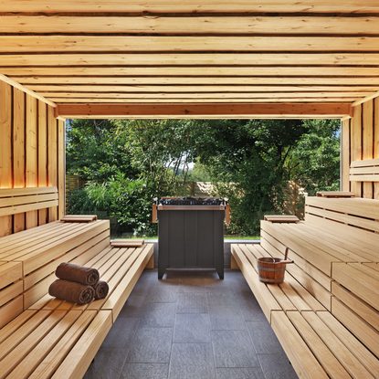 Innenansicht einer Holzsauna mit Sitzbänken, Saunaofen und offenem Blick in den Garten.