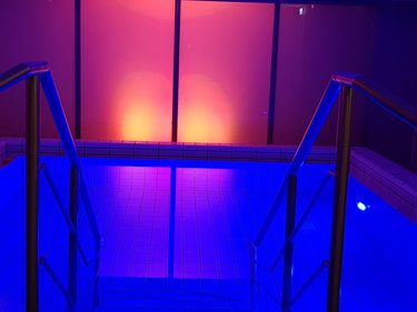 Beleuchtetes Indoor-Wellnessbecken mit Treppe, Handläufen und blau-violetter Lichtstimmung.