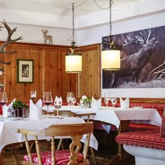 Rustikaler Restaurantbereich mit gedeckten Tischen, Holzvertäfelung und Hirschbild an der Wand.