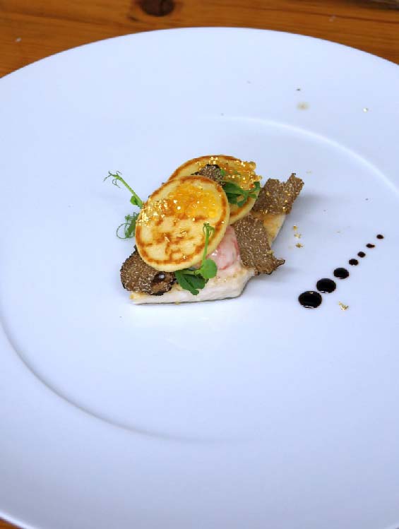 Kunstvoll angerichtete Gourmet-Vorspeise auf einem weißen Teller mit Trüffelscheiben, Mini-Pfannkuchen, Blattgold und feinen Garnierungen; dekorative Balsamico-Tropfen am Tellerran